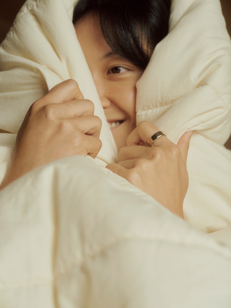 A smiling woman wrapped in a white comforter while wearing Auro Ring 5 in gold