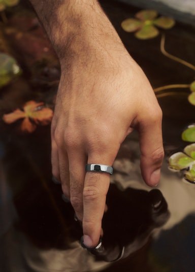 A hand wearing an Auro Ring 5 touching the surface of a pond
